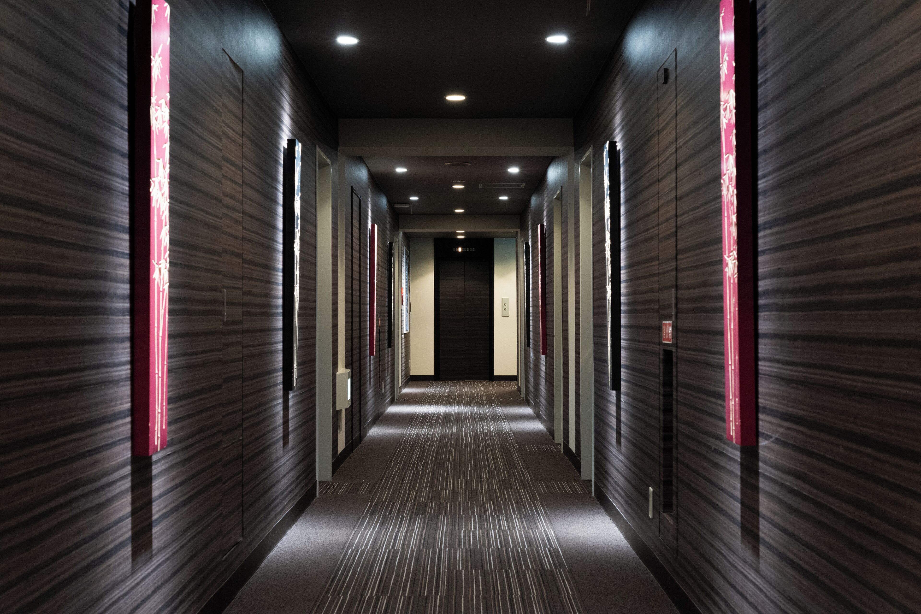 A corridor with a patterned floor, dark walls, and red vertical light strips.