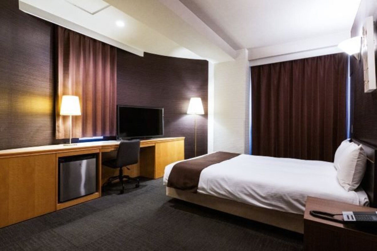 A hotel room with a bed, desk, television, and two lamps.