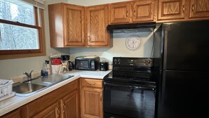 Eine Küche mit Holzausstattung, einem schwarzen Kühlschrank, einer Mikrowelle, einem Toaster und einer Wanduhr.