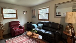 Ein Wohnzimmer mit einem roten Ledersessel, einer schwarzen Ledersofa, einem Couchtisch aus Holz mit einer Pflanze und einem roten Teppich mit Muster.