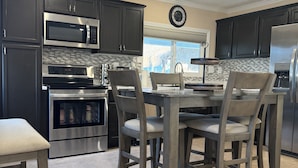A modern kitchen with dark cabinets, stainless steel appliances, a dining table with chairs, and a large window. - La Casita, Las Vegas (Las Vegas)