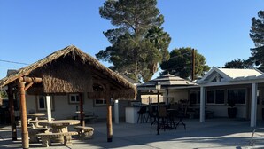 A pool area with a thatched gazebo, outdoor seating, and a building with large windows. - La Casita, Las Vegas (Las Vegas)