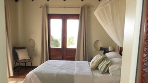 Ein Schlafzimmer mit Bett, Stuhl, Deckenventilator und Fenster mit Vorhängen.
