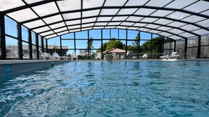 Ein Hallenbad mit Glasdach, Liegestühlen und Blick auf die Umgebung.