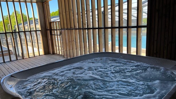 Ein Whirlpool mit Holzterrasse und Metallgeländern, mit Blick auf einen Pool und Grünflächen.