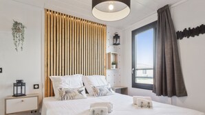 Ein modernes Schlafzimmer mit einem großen Bett, einem Nachttisch, einem Beistelltisch, einem Fenster mit Vorhängen und einer hängenden Pflanze.