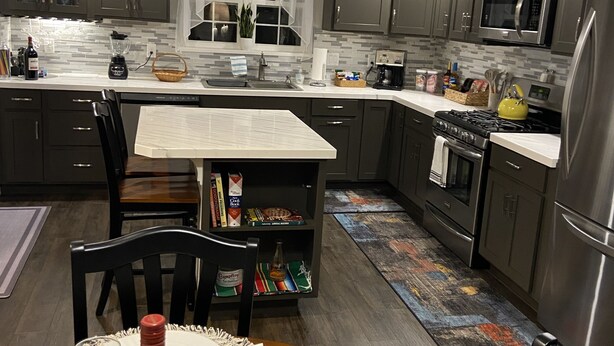 Une cuisine moderne avec des meubles de couleur sombre, un four à micro-ondes, une cuisinière et un coin repas comprenant une table, des chaises et une bouteille de vin.