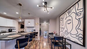 Una cocina moderna con una isla central, taburetes de bar y un comedor con una gran obra de arte abstracta en la pared.