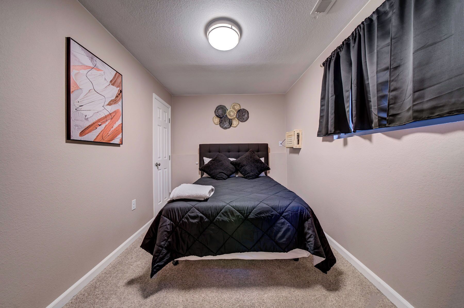 A bedroom with a bed, a ceiling light, a door, and a wall decoration.