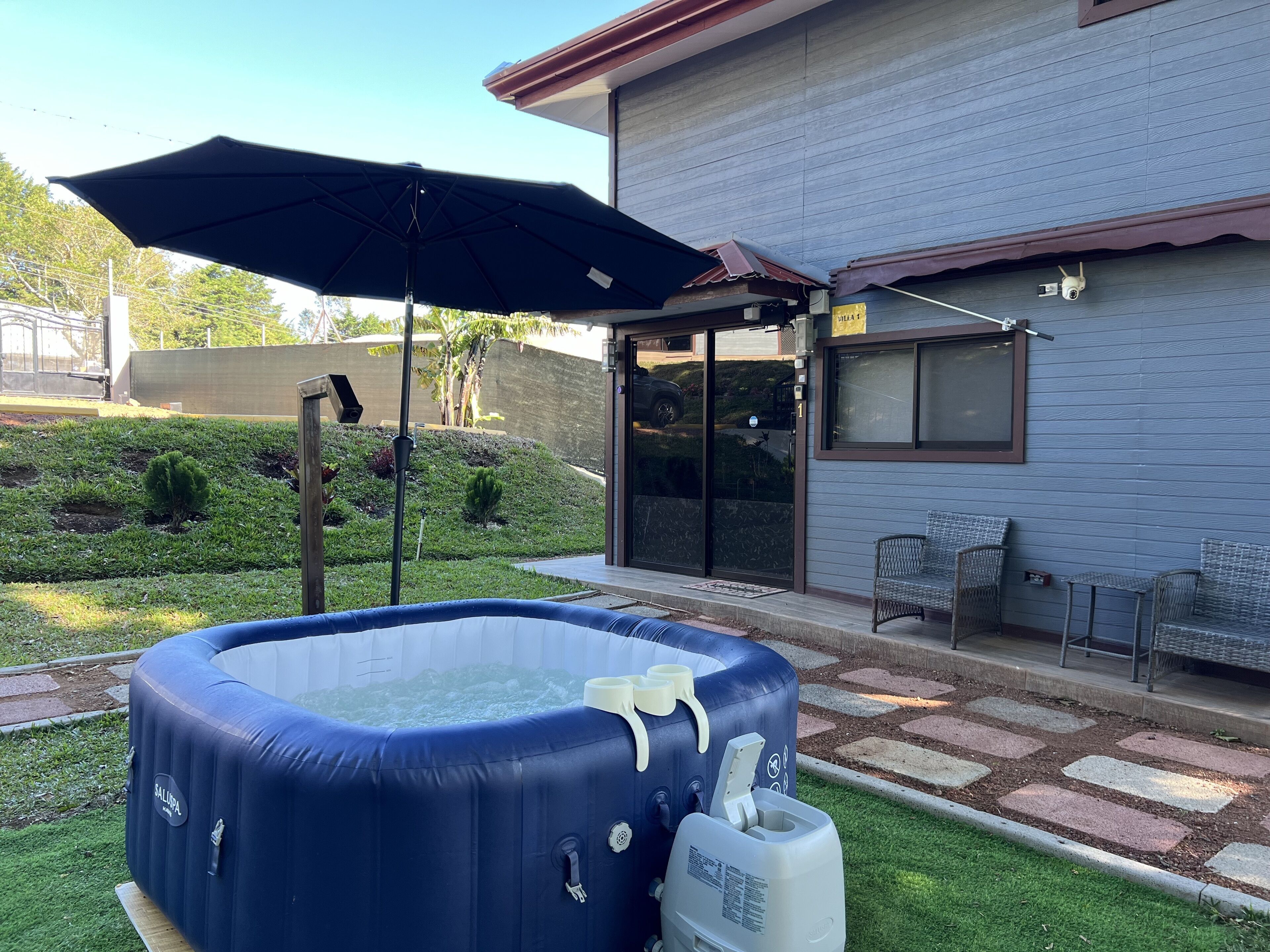 An outdoor hot tub with a blue cover, a large umbrella, and a water heater.