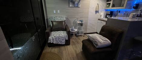 A compact living space with a sofa, a chair, a small table, a microwave, and a dishwasher.