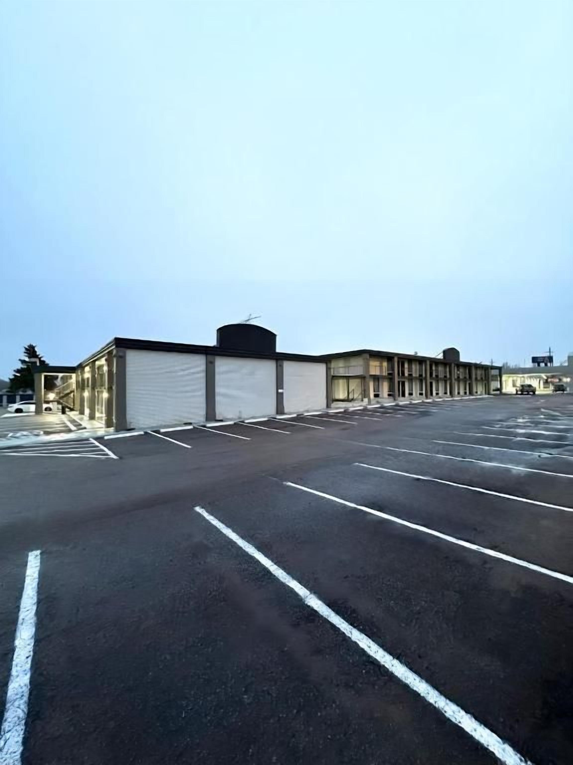 A parking lot with marked parking spaces and a building with a white facade and large windows.
