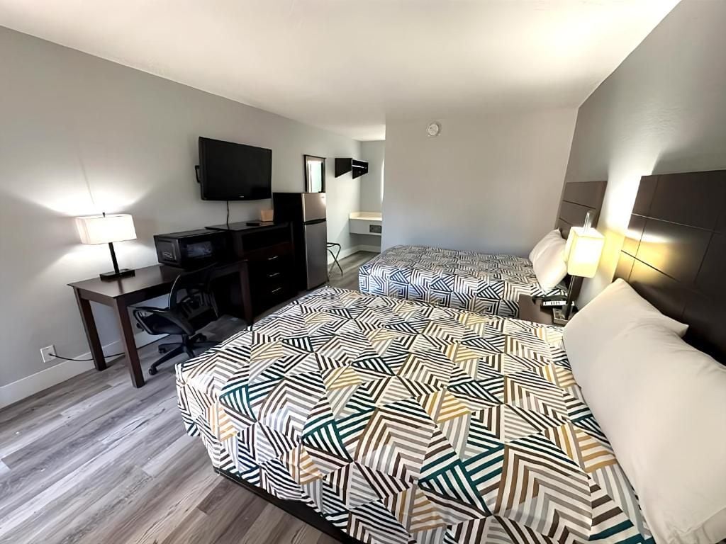 Ein Hotelzimmer mit zwei Betten, einem Schreibtisch, einem Fernseher und einem Sessel.