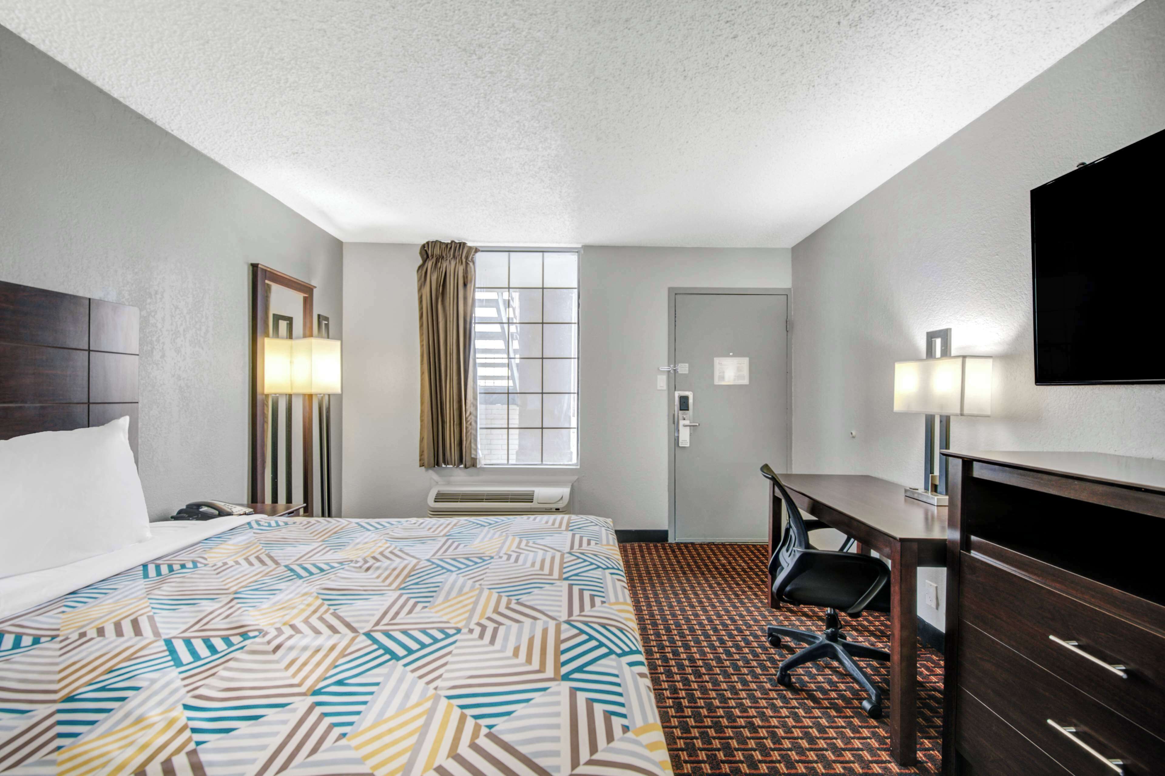 Habitación de hotel con cama, escritorio, silla y televisión.
