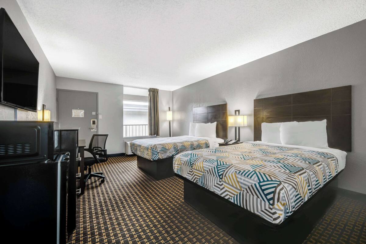 A hotel room with two beds, a desk, a TV, and a window with curtains.