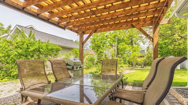 An outdoor patio with a glass-top table and four chairs, surrounded by a wooden pergola.