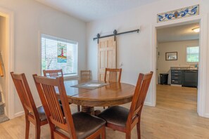 A dining area with a round wooden table, six wooden chairs, and a stained glass window with a lighthouse design.