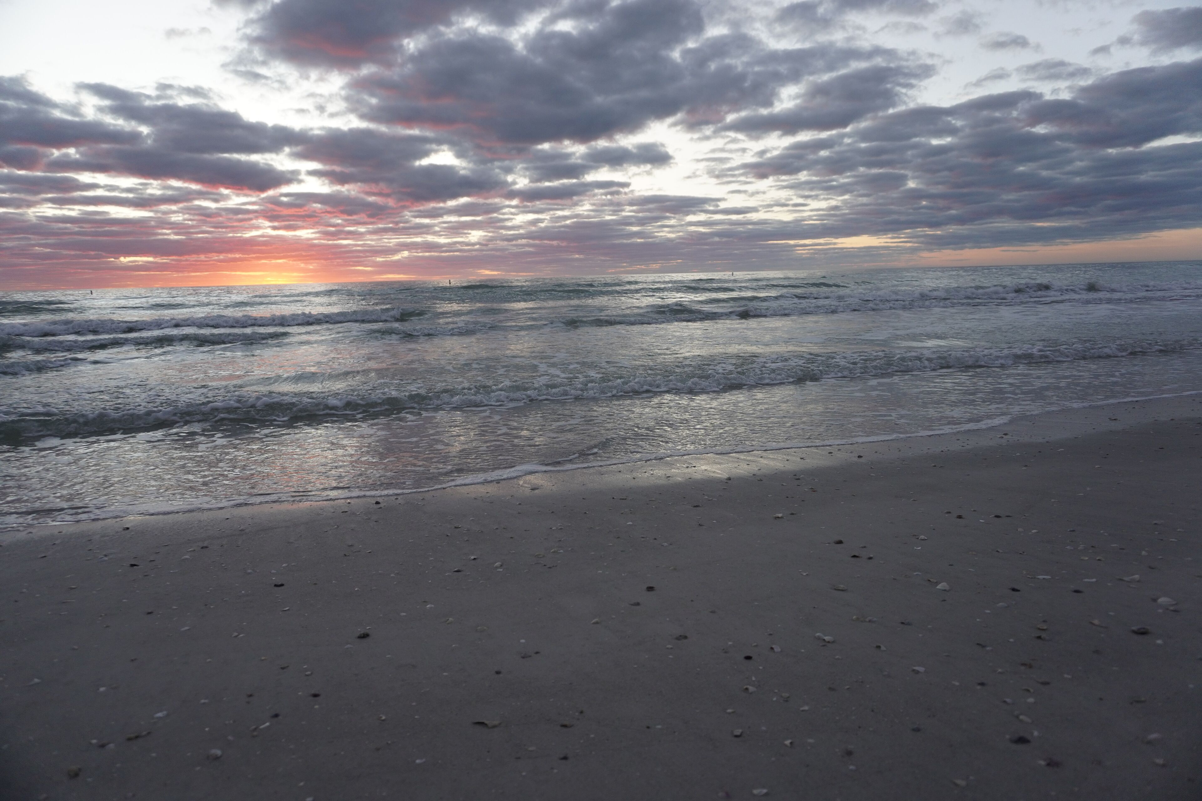 A beach with a sunset and ocean waves.