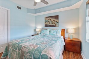 A bedroom with a bed, nightstands, a ceiling fan, and a wall-mounted artwork.