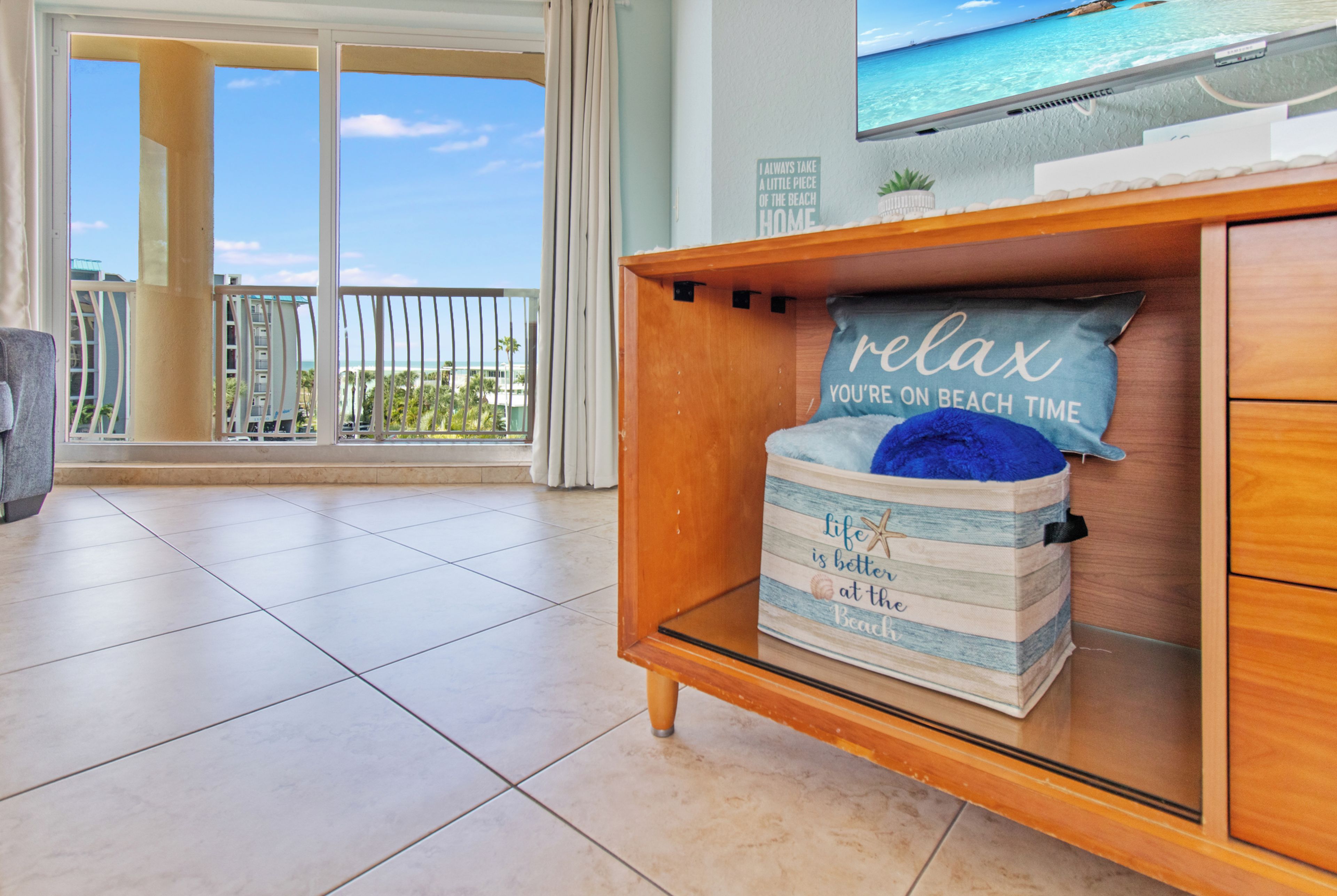 A room with a wooden cabinet, a beach-themed pillow, and a large window with a view of the ocean.