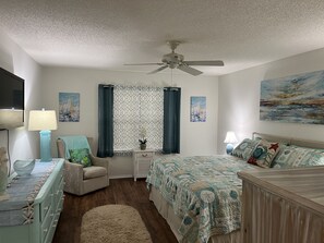 A bedroom with a bed, a chair, a desk, a ceiling fan, and artwork on the walls.