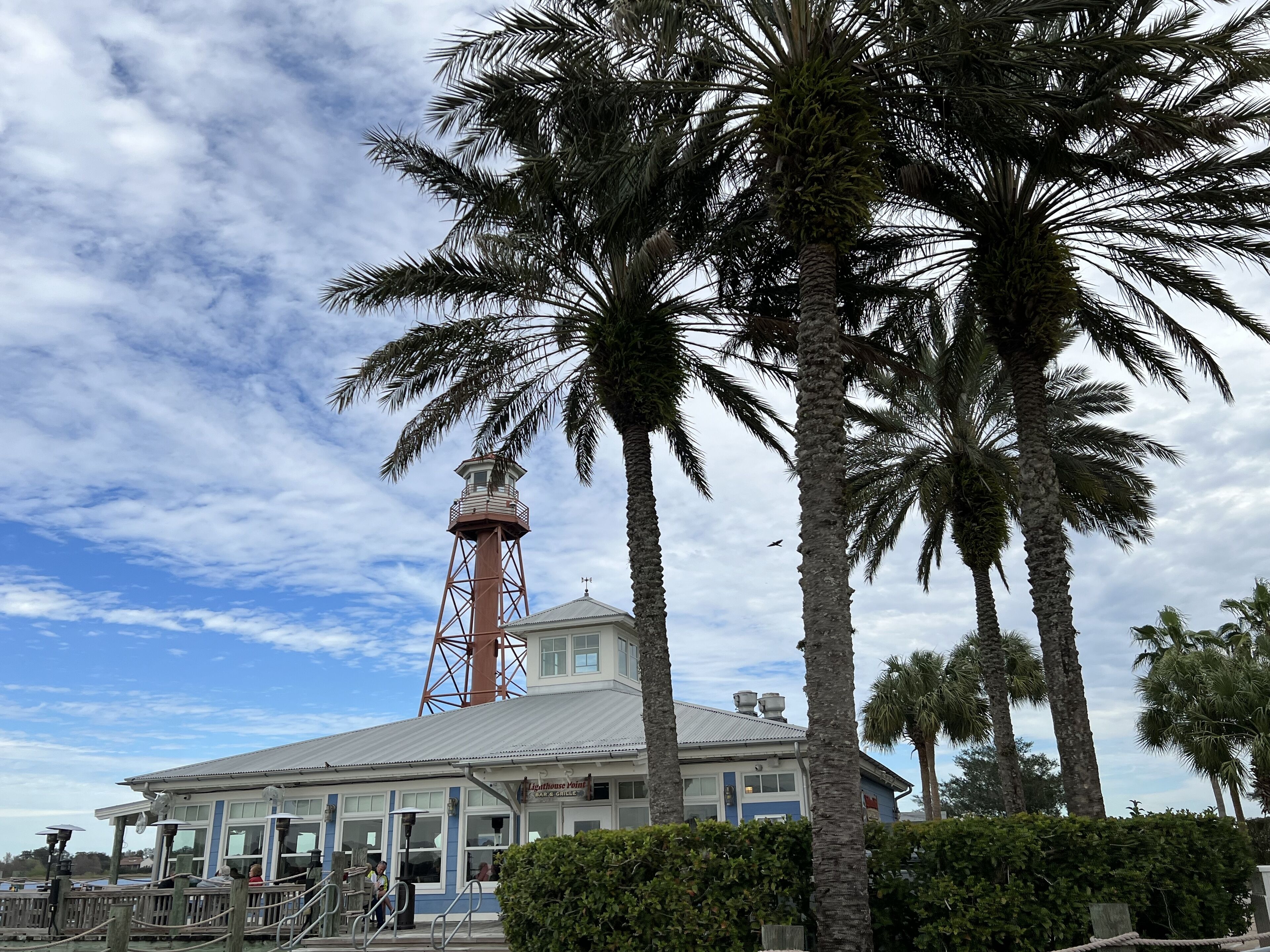 Un phare avec un bâtiment blanc au premier plan, des palmiers et un ciel dégagé.