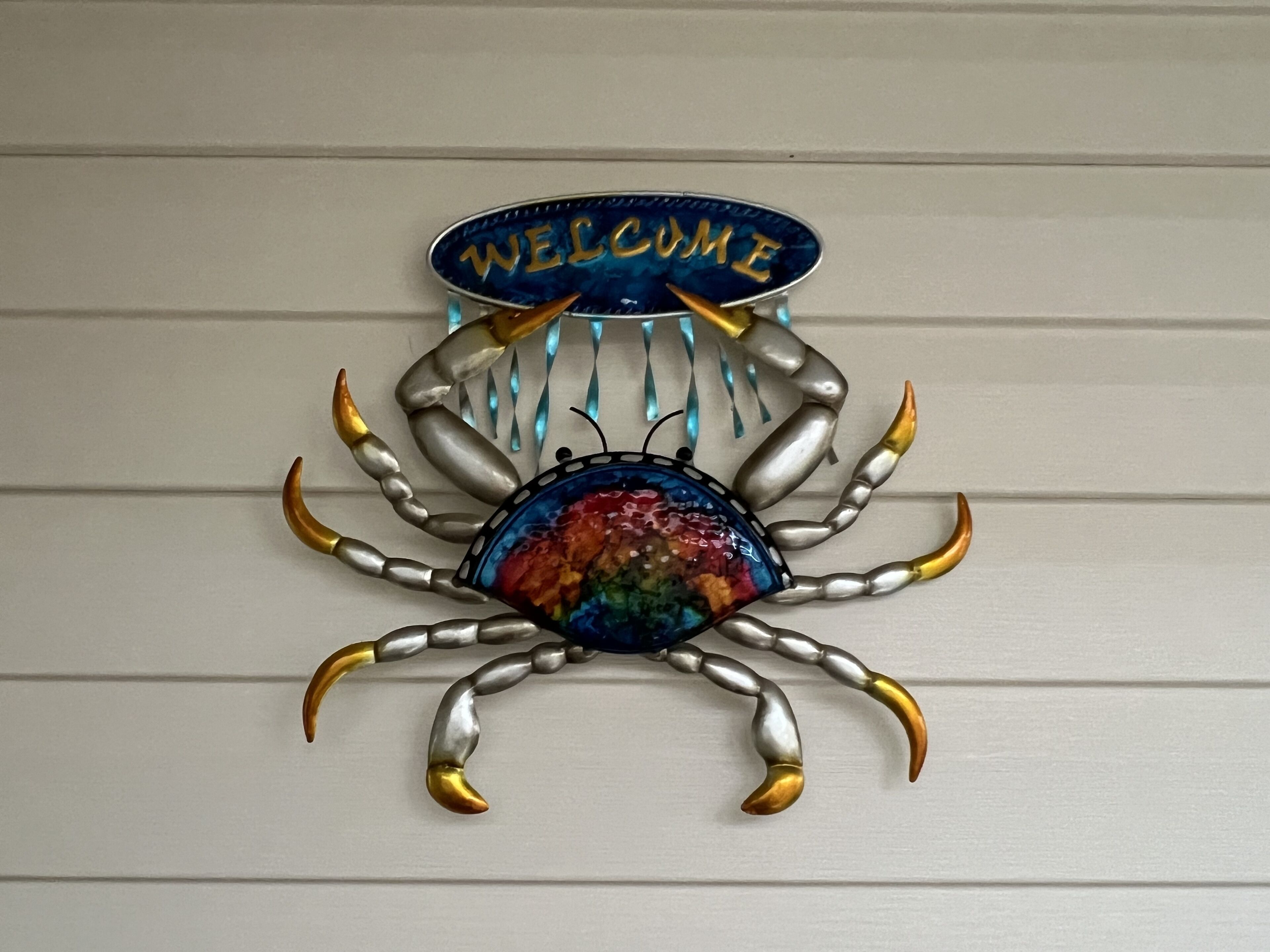 A decorative crab with a 'WELCOME' sign on its back, set against a white wall.