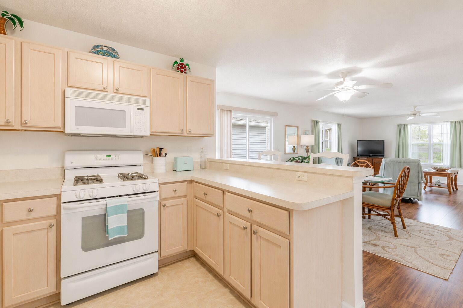 A kitchen with a microwave, stove, and cabinets, a dining area with chairs and a table, and a ceiling fan.