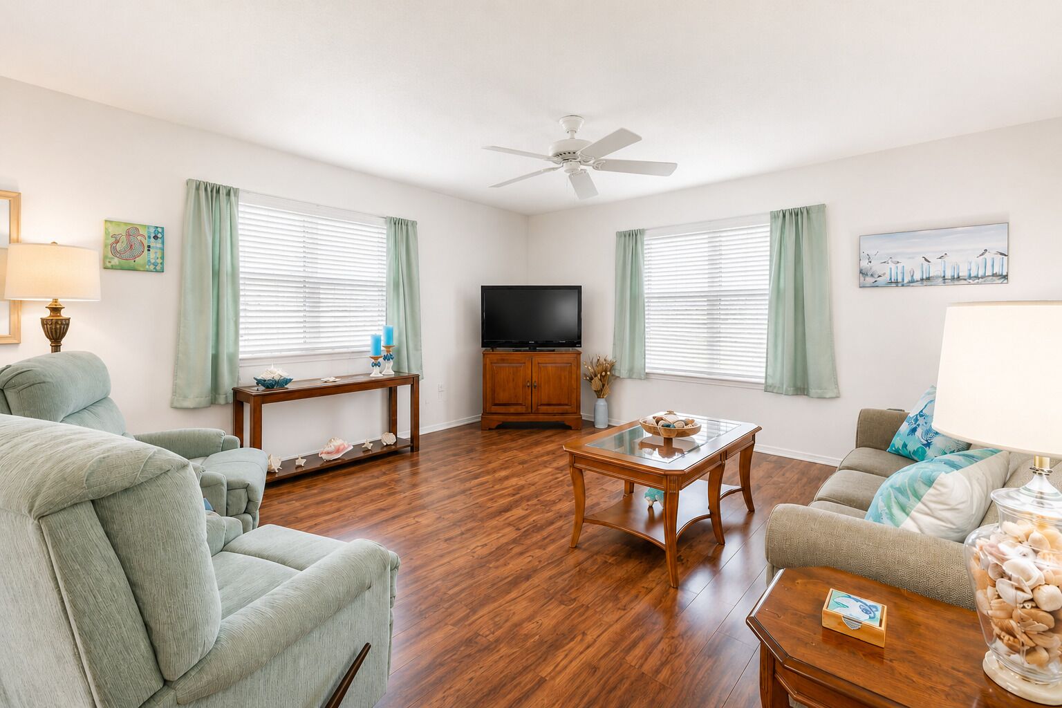 A living room with a sofa, a coffee table, a TV stand, and a ceiling fan.