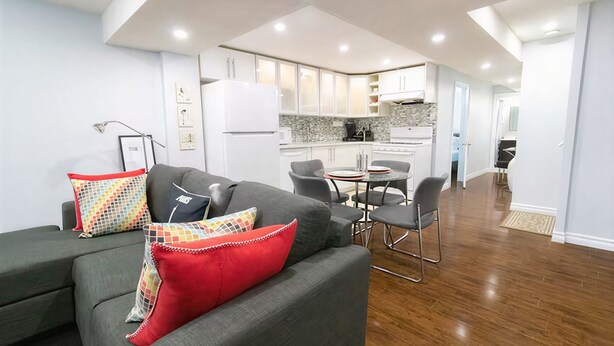 A modern living room with a grey sofa, colorful cushions, and a dining area with a small table and chairs. - Modern Cozy 2 BR Private Suite,5 Min drive -Creditview & Sandalwood Sports field (Brampton)