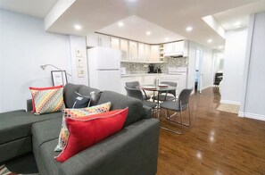 A modern living room with a grey sofa, colorful cushions, and a dining area with a small table and chairs.