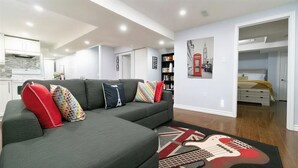A modern living room with a sectional sofa, a guitar-themed rug, and a bookshelf. - Modern Cozy 2 BR Private Suite,5 Min drive -Creditview & Sandalwood Sports field (Brampton)