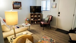 A living room with a sofa, a table, a TV, a bookshelf, and a chair. - Just a walk to the beach, centrally located, multiple pools, family friendly. (Hilton Head Island)