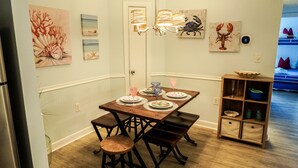 A dining area with a wooden table set for four, surrounded by chairs. There are wall-mounted paintings and a chandelier above the table. - Just a walk to the beach, centrally located, multiple pools, family friendly. (Hilton Head Island)