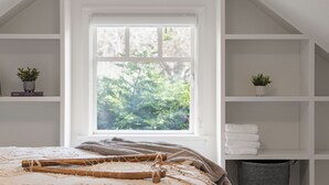 Een slaapkamer met een groot raam, een bed met een houten hoofdbord en witte open kasten.