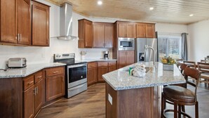 Une cuisine moderne dotée de meubles en bois, d’appareils électroménagers en acier inoxydable, de plans de travail en granit et d’un îlot central agrémenté de tabourets de bar.