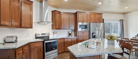 A modern kitchen with wooden cabinets, stainless steel appliances, granite countertops, and a central island with bar stools.