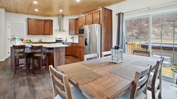 Une cuisine spacieuse avec des meubles en bois, un îlot central doté de tabourets, une grande table à manger et une vue dégagée grâce à une porte-fenêtre coulissante.