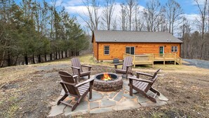 Une cabane en rondins avec un foyer et un espace extérieur aménagé pour s’asseoir.
