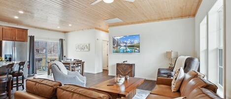 Un salón espacioso con sofás de cuero, una mesa de comedor de madera y un televisor de pantalla plana grande montado en la pared.