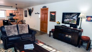A living room with a dark leather sofa, a wooden coffee table, and a television on a wooden stand. - Condo Overlooking Fall River (Estes Park)