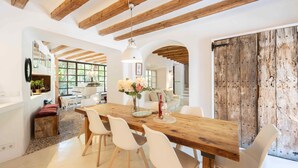 A dining area with a wooden table, white chairs, and a hanging light fixture. - Es Clot (Deia)