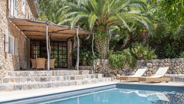 A pool area with lounge chairs, a covered seating area, and a stone wall. - Es Clot (Deia)