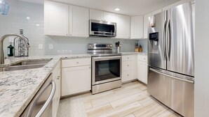 A modern kitchen with white cabinets, stainless steel appliances, a built-in oven, and a refrigerator. - Shared Pool, Golf Cart Boardwalk, Shared Grills (Port Aransas)
