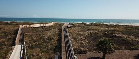 A coastal boardwalk with a clear view of the ocean and beach.