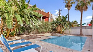 A swimming pool with lounge chairs, surrounded by tropical plants and a wooden deck. - Private Home w/Private pool1/2 block from Beach! Stylish Interior! Dog friendly! (South Padre Island)