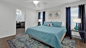 A bedroom with a bed, a ceiling fan, a nightstand with a lamp, and a window with curtains. - Private Home w/Private pool1/2 block from Beach! Stylish Interior! Dog friendly! (South Padre Island)