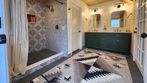 Ein Badezimmer mit Holzboden, Wand mit geometrischem Muster, grünem Waschtisch und einem gemusterten Teppich.
