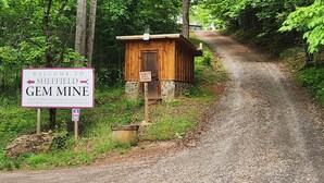 Eine Holzhütte mit dem Namen 'Ruby's Gem Cabin', mit einem Schild, das 'Willkommen bei Sheffield Gem Mine' und die Öffnungszeiten anzeigt.
