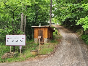 A wooden cabin labeled 'Ruby's Gem Cabin' with a sign indicating 'Welcome to Sheffield Gem Mine' and operational hours.